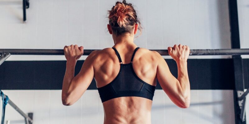 Athletic woman doing a pull-up in a gym, showing defined back muscles and strength