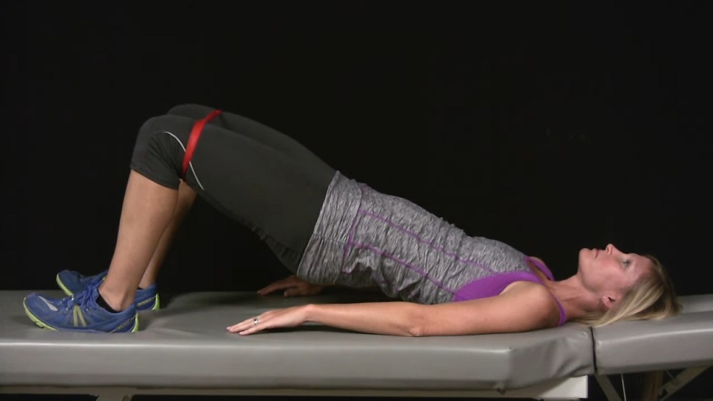 Woman holding a glute bridge pose on a flat bench, knees apart and hips raised