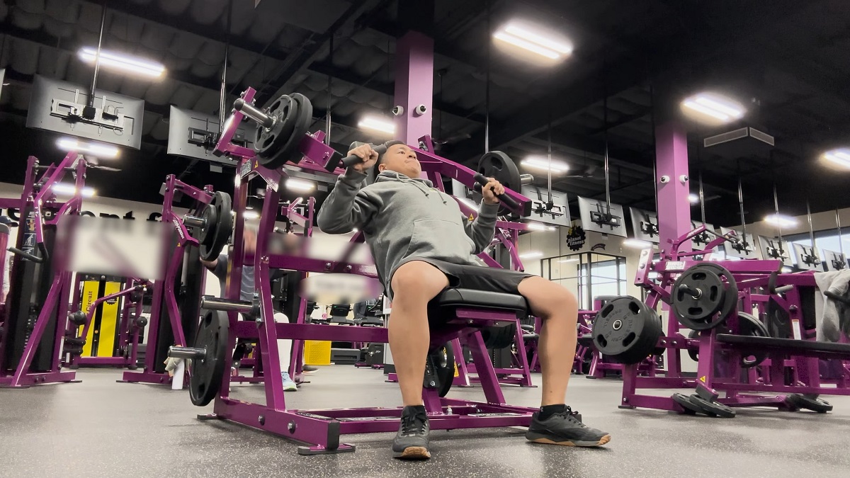 Person using a chest press machine in a gym setting, wearing a hoodie