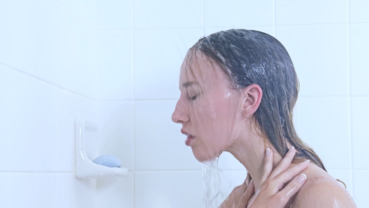 A woman taking a shower, letting water rinse over her face and shoulders