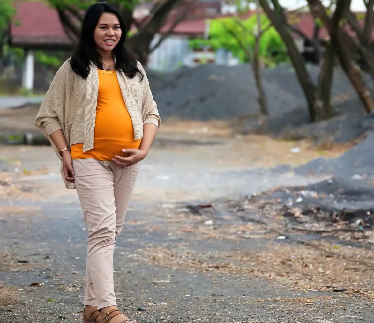 A smiling woman in a mustard-yellow top and beige cardigan walks along an outdoor path