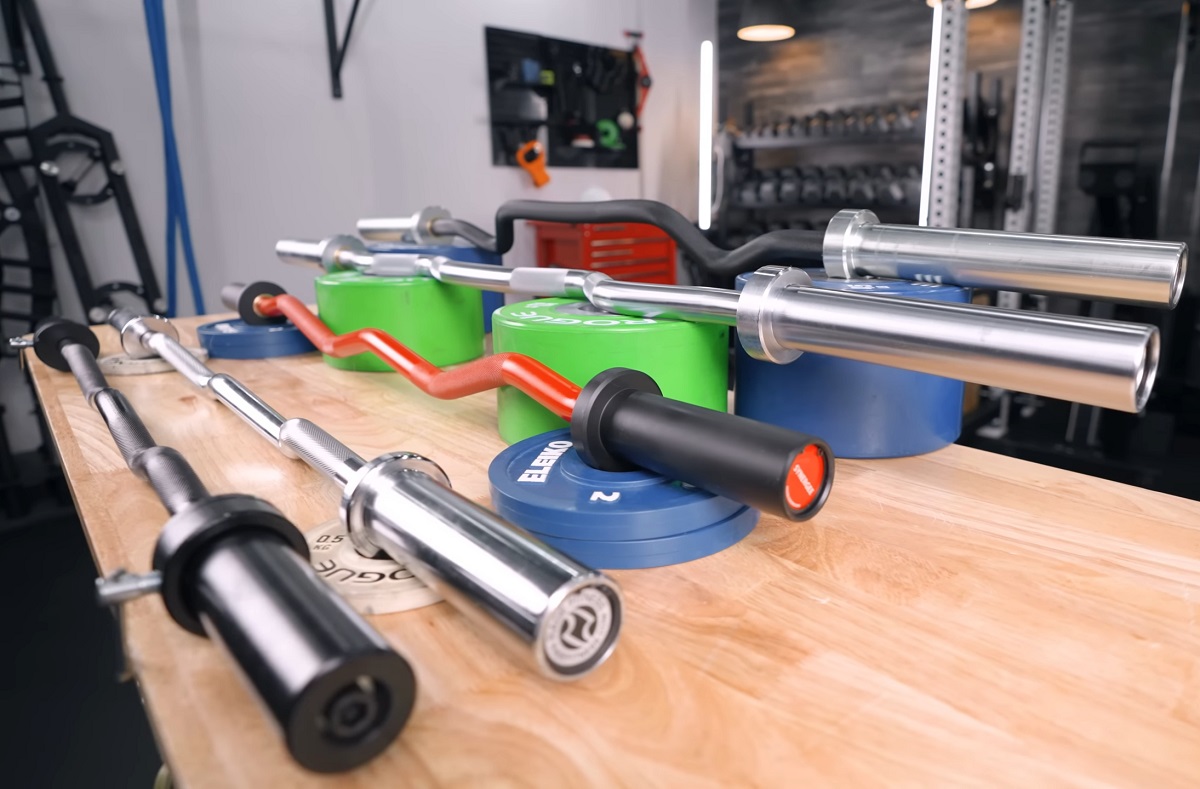 Various weightlifting EZ curl bars displayed on a table in a gym setting, showcasing different grip and lifting options