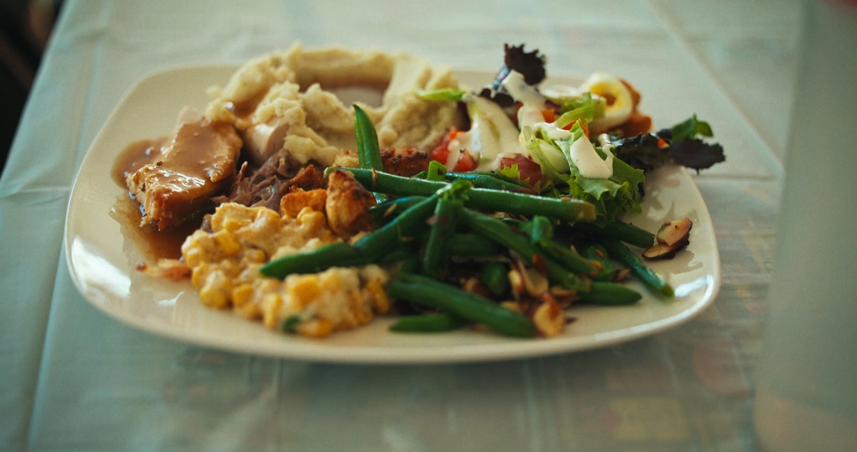 A plate filled with mashed potatoes, turkey with gravy, green beans, salad, and corn casserole on a table