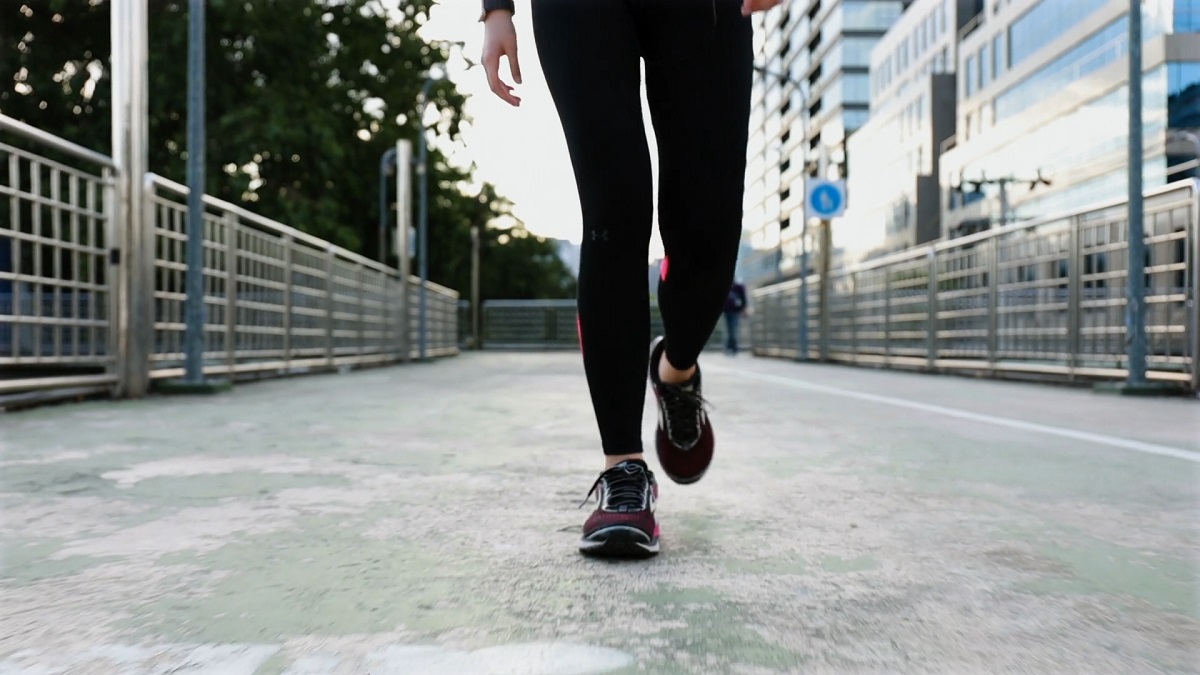 A close-up shot of a person walking on an urban bridge, dressed in athletic wear and sneakers, emphasizing movement and cardiovascular exercise