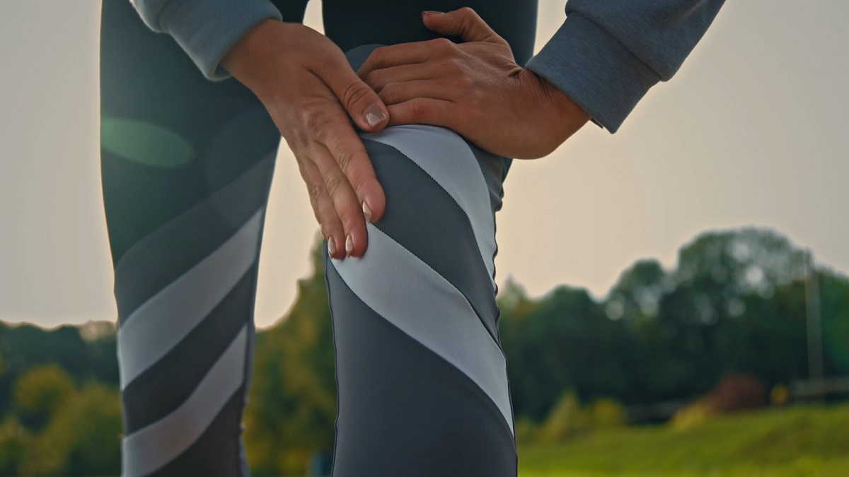 A close-up of a person holding their knee in discomfort while wearing workout leggings, highlighting the importance of joint-friendly cardio exercises