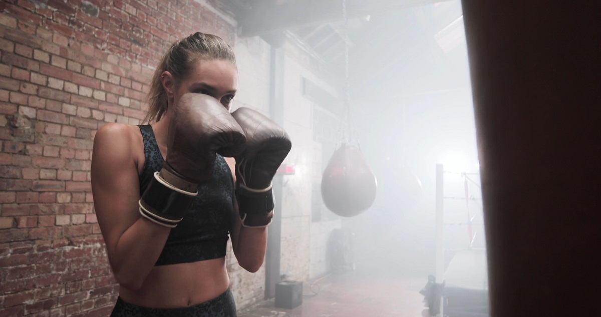 A determined woman wearing boxing gloves in a smoky gym