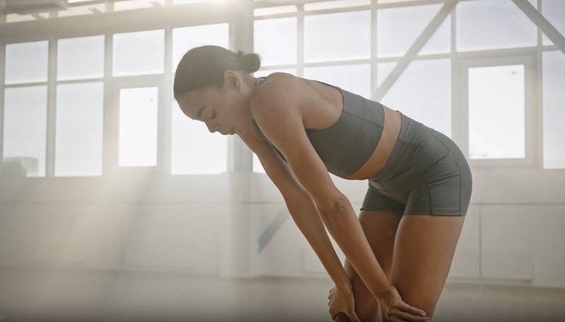 Exhausted athlete, leaning forward, seeking respite in a sun-drenched studio