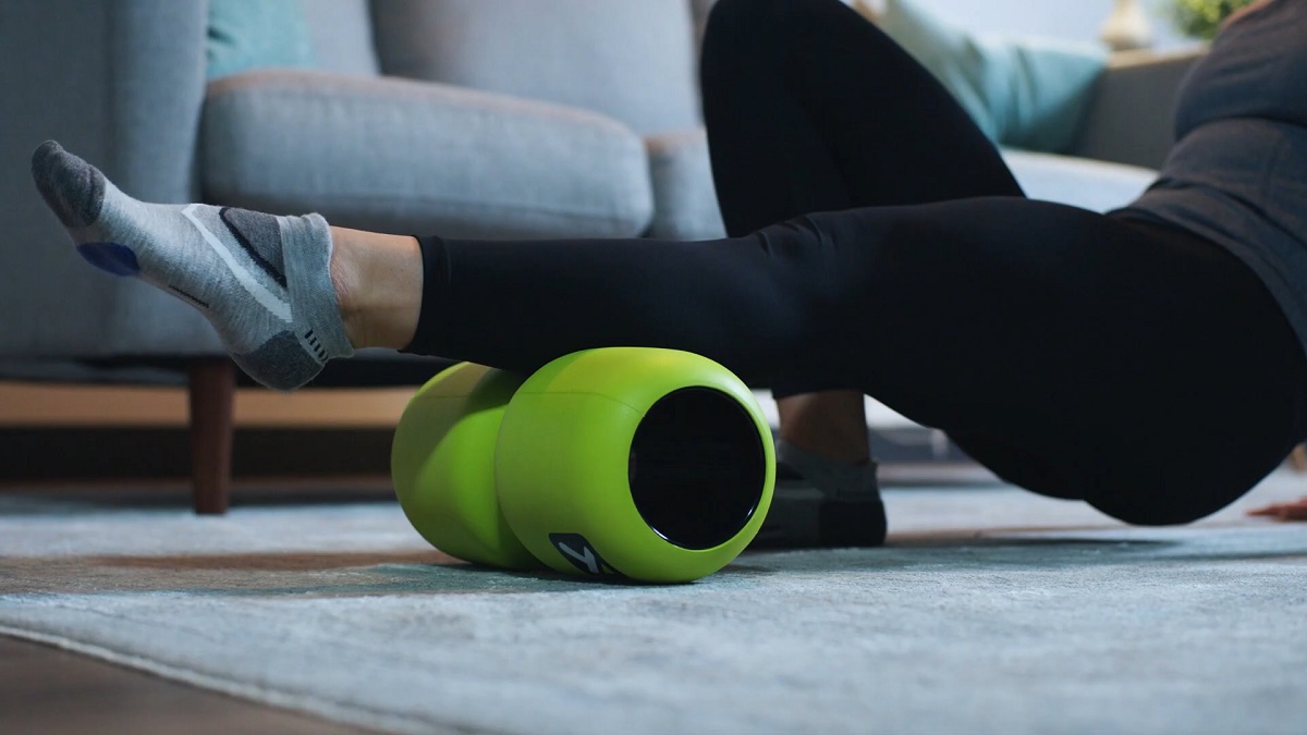 A person using a bright green foam roller to massage their leg muscles on a carpeted floor