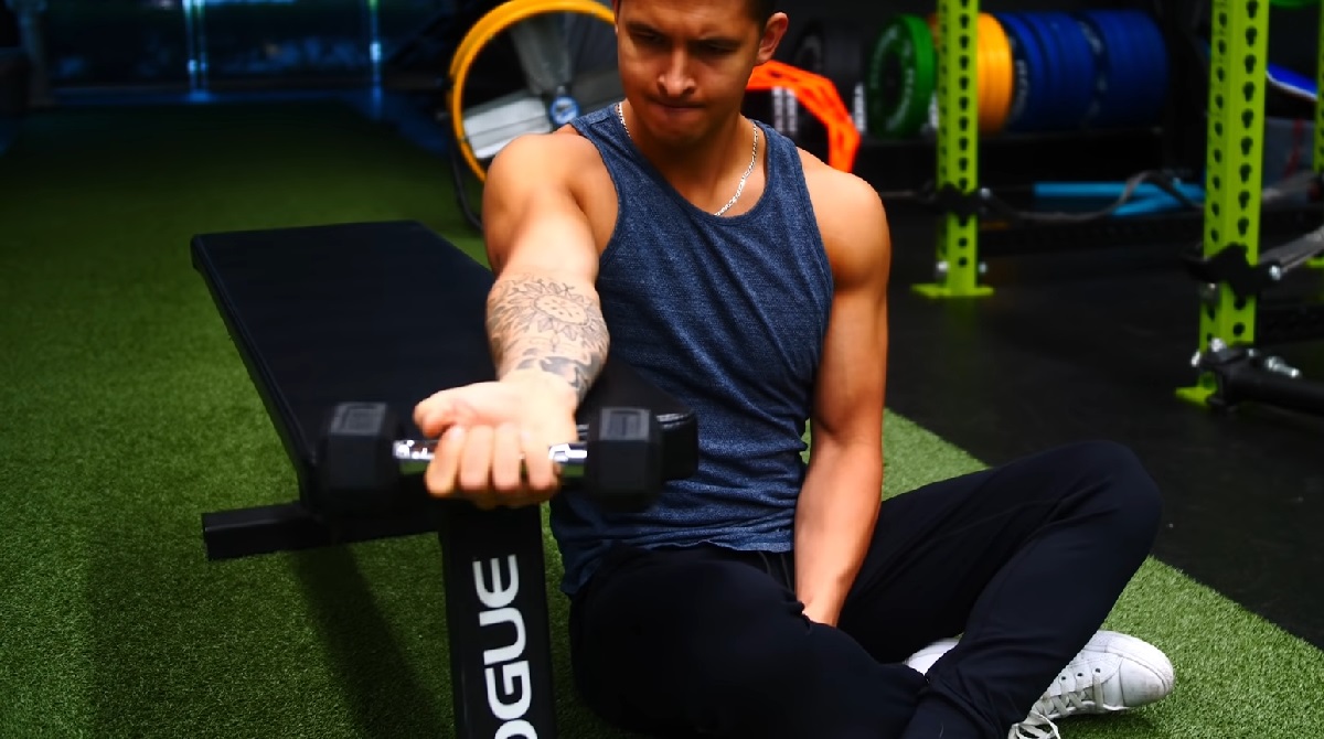 A man performing a seated wrist curl exercise with a dumbbell in a gym, focusing on strengthening his forearm muscles