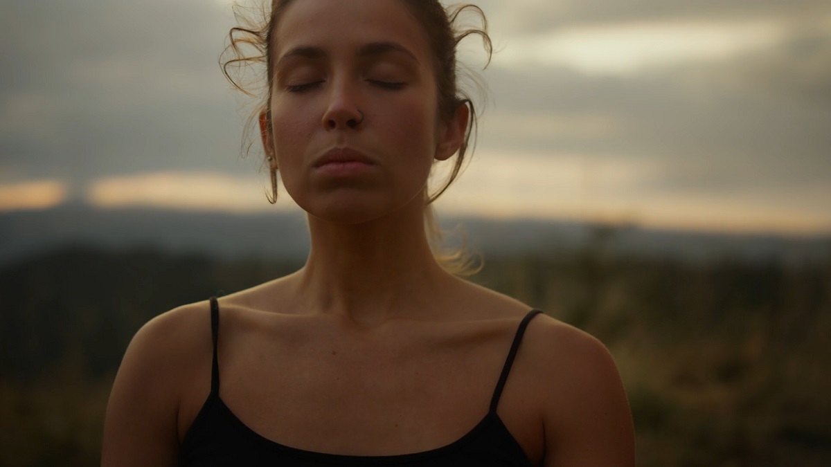 A woman with her eyes closed, standing outdoors at sunset, practicing deep breathing and visualization techniques for relaxation