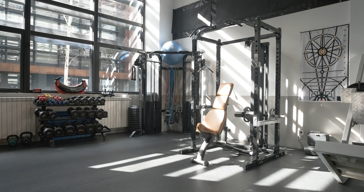 A well-equipped gym corner with free weights, a power rack, resistance bands, and a workout bench