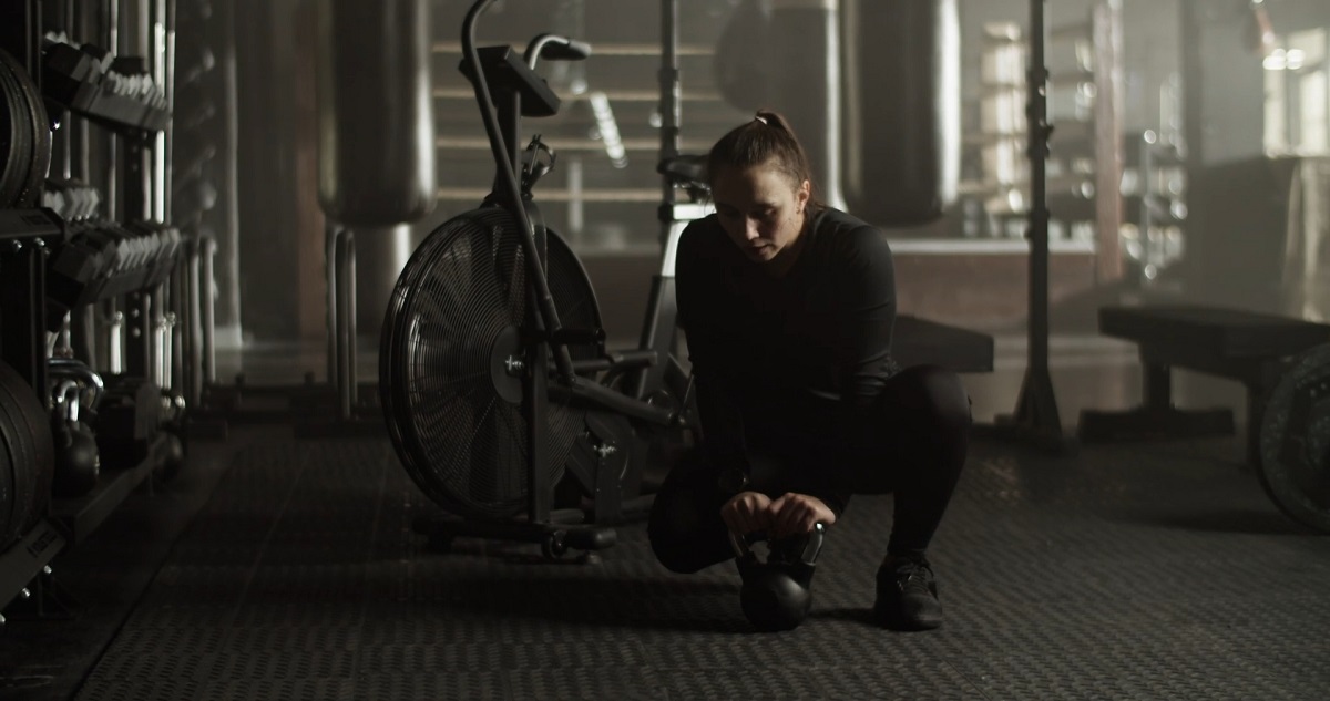 A woman in a black workout outfit kneeling in a gym