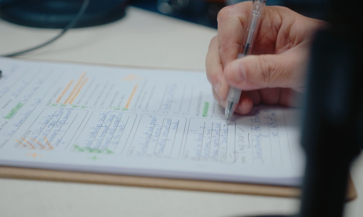 A close-up of a person’s hand writing on a clipboard with a pen, highlighting notes and information