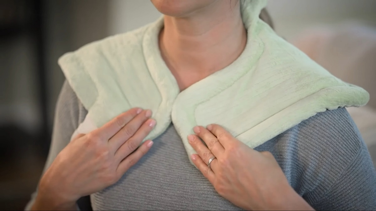  A woman placing a soft, heated neck wrap around her shoulders for relaxation