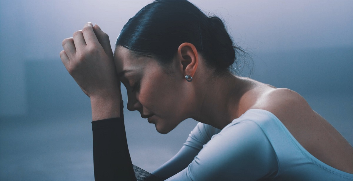 A woman sitting with her head resting on her hands, appearing deep in thought, embodying the importance of being kind to oneself