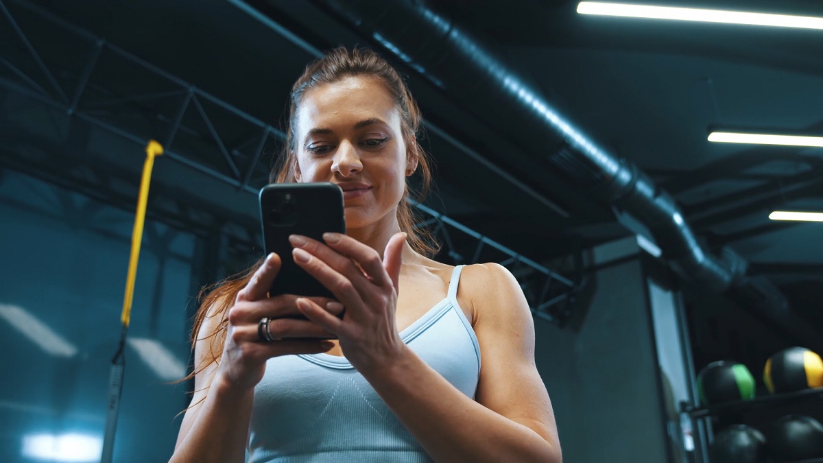  A woman in a gym, dressed in a light blue sports outfit, holding and looking at her smartphone