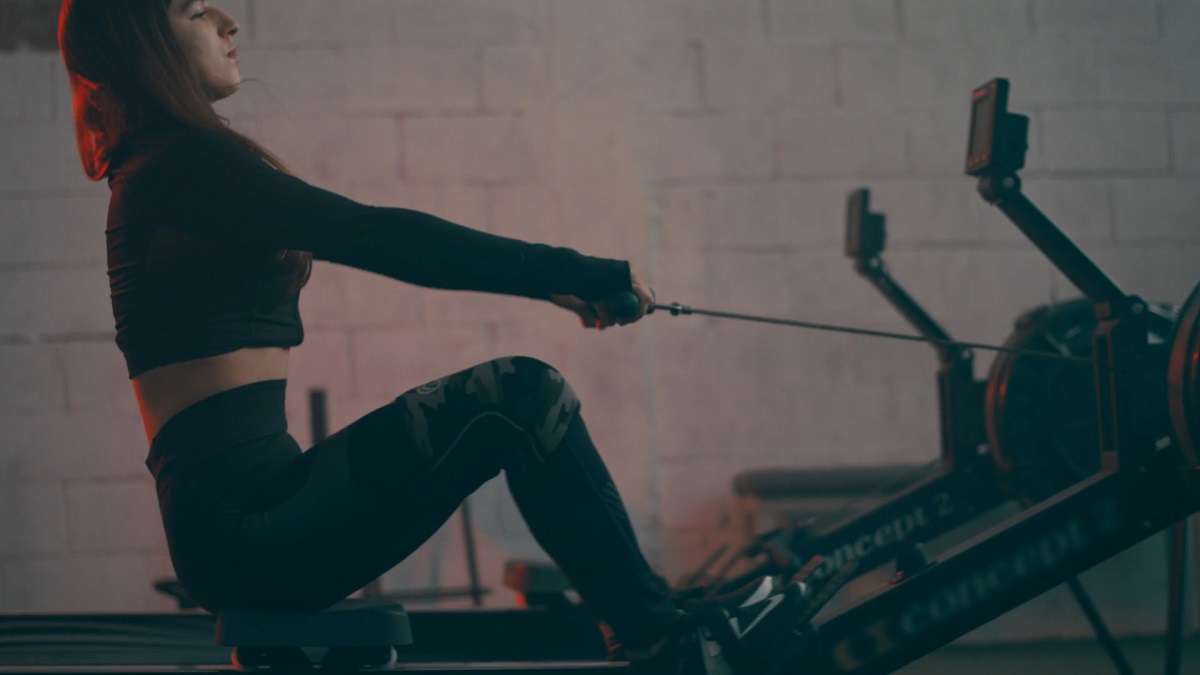 A woman in a dimly lit gym using a rowing machine for a full-body cardio workout