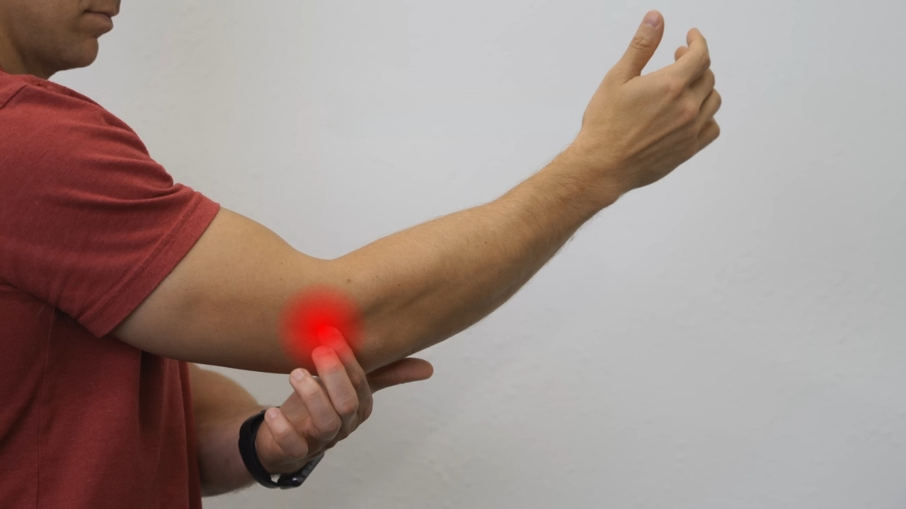 A person touching their inner elbow with redness indicating pain, suggesting symptoms of tendonitis or repetitive strain injury