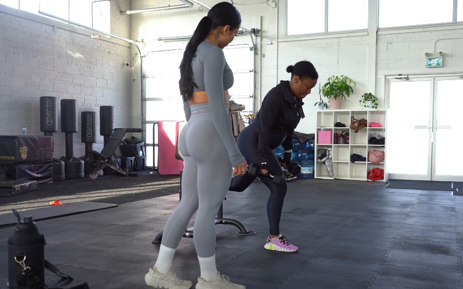 Woman doing dumbbell rows with trainer in modern gym setting