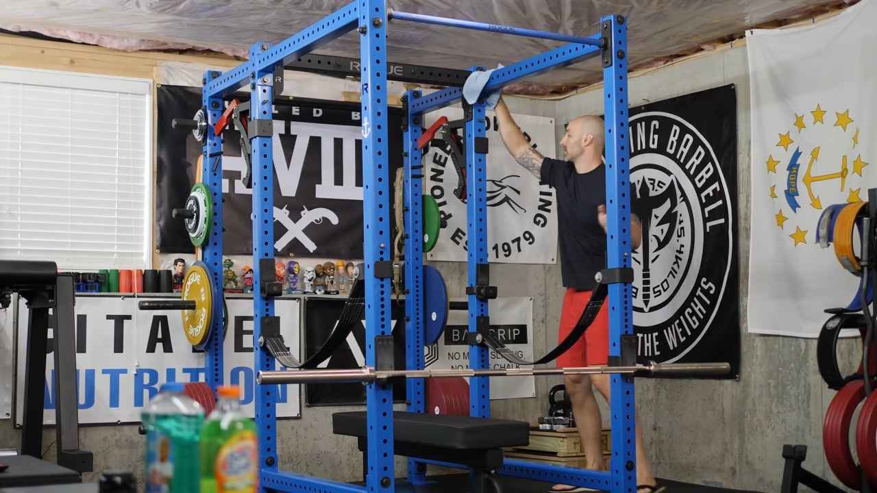 Person cleaning a power rack in a home gym with banners and equipment around