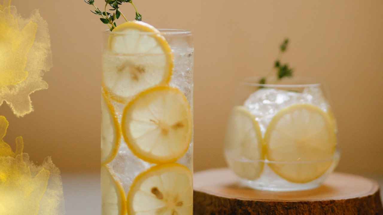 Glasses of lemon water with ice and thyme on a wooden surface