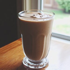 A tall glass filled with a creamy vanilla chai smoothie, placed on a wooden table near a window with natural light