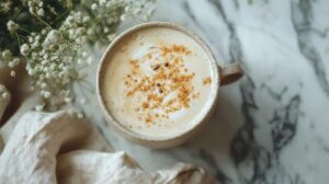 A ceramic mug filled with a creamy chai latte, sprinkled with spices, placed on a marble surface with soft linen and delicate flowers