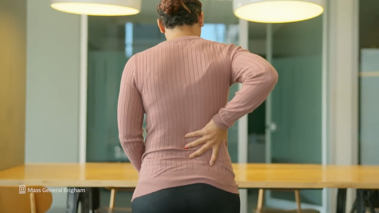 Woman standing in an office, pressing her lower back in discomfort.