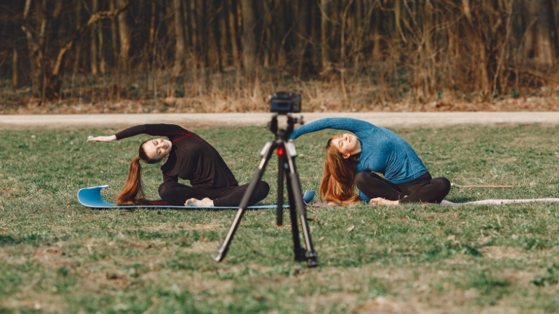 Two women doing outdoor yoga recorded by an action camera mounted on a tripod