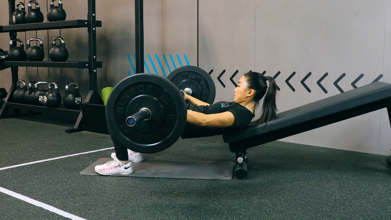 A person performing a barbell hip thrust on a bench