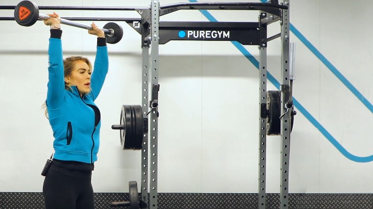 Woman performs a barbell overhead press in a gym