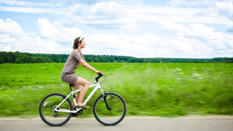 A woman cycling along a rural road, enjoying fresh air and movement that help raise dopamine levels