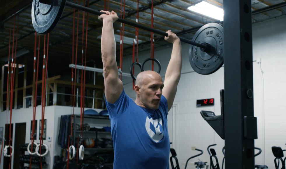 The gym's interior provides a backdrop for the powerful barbell press