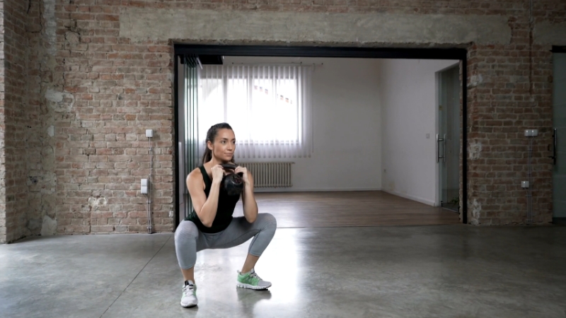 Woman performing a squat with a kettlebell in a spacious workout space