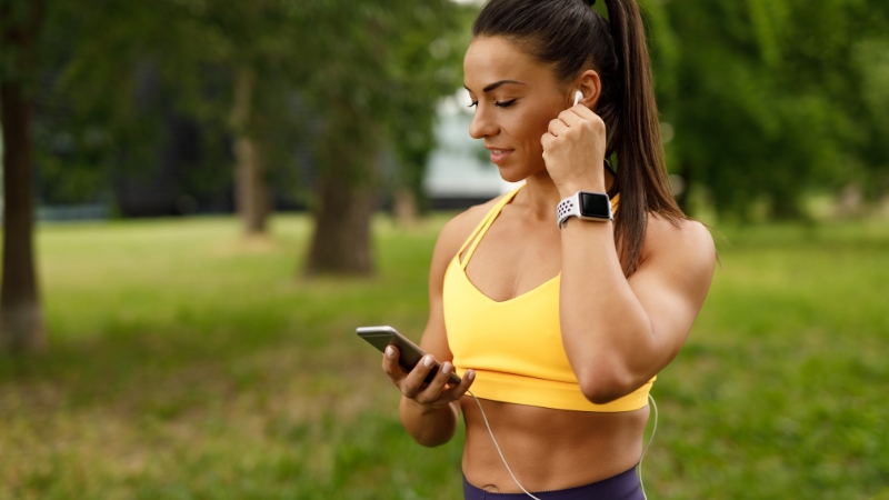 Woman in workout gear using earphones and a phone during outdoor training in a park