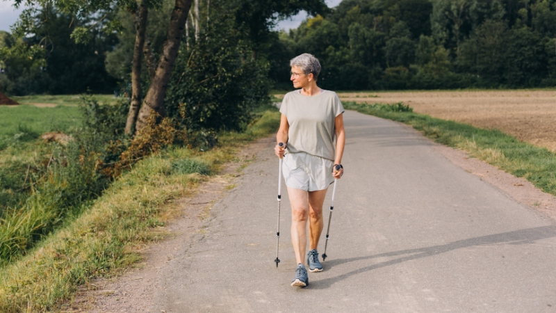 Older woman walking with poles on a rural path as part of an active lifestyle after 65