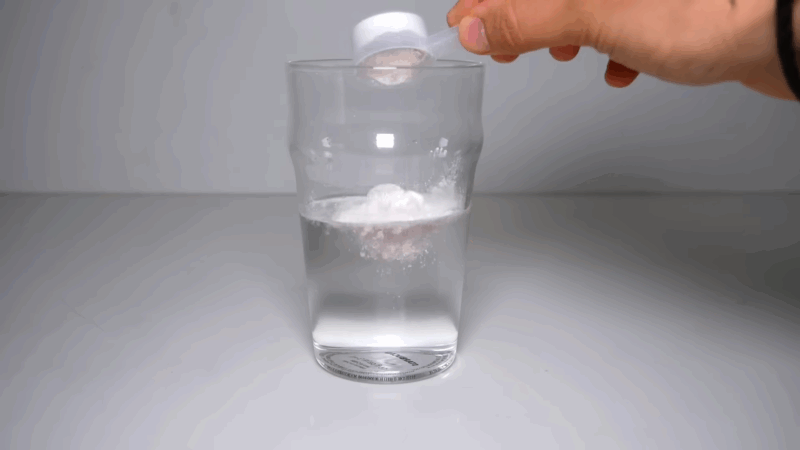 A person adding a scoop of pre-workout powder to a glass of water