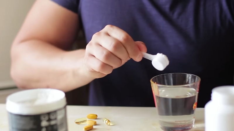 A person adding pre-workout powder to a glass of water while surrounded by supplements