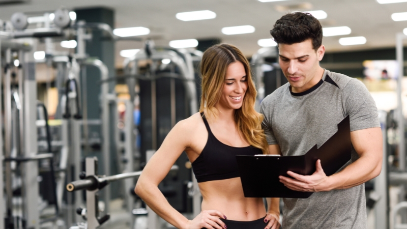 A personal trainer reviews a custom plan with a client in a gym, highlighting key fitness specializations for tailored results