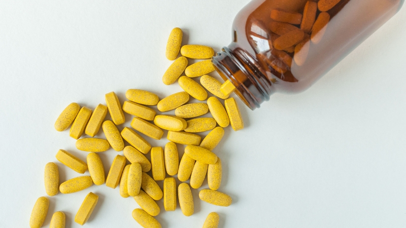 Yellow multivitamin tablets spilled from a brown bottle onto a white surface
