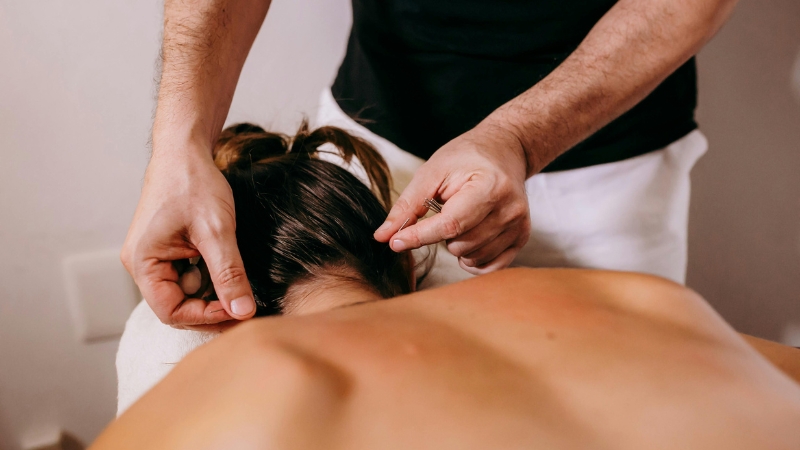 A woman receives acupuncture on her upper back and neck to relieve neck pain