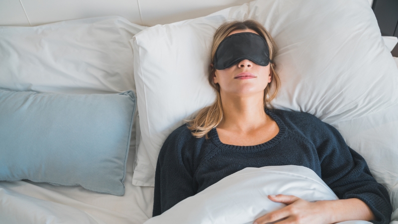 Woman sleeping on her back with an eye mask and proper pillow support to promote neck alignment
