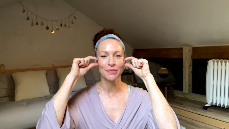 Woman performing cheekbone lift face exercises by pressing her fingers into the sides of her face