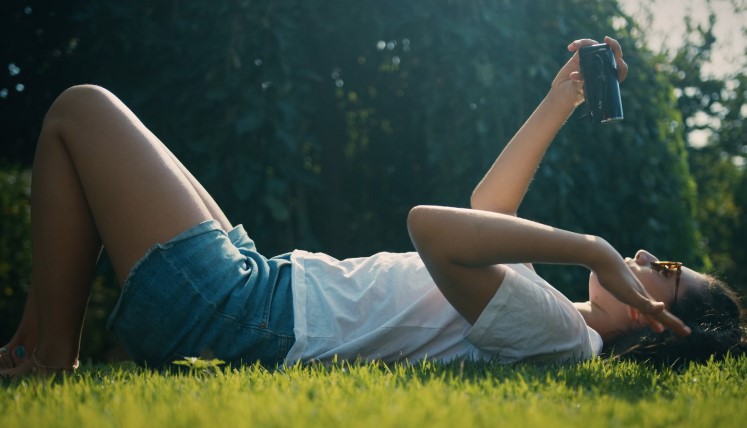 A young woman relaxes on a grassy field, taking a selfie