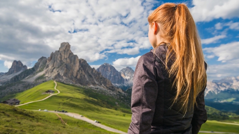 Woman in trekking gear looks toward rugged mountain peaks, highlighting essential gear for trekking at high altitudes