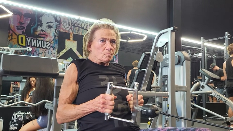 Marlene Flowers performs a seated row exercise with focus and control at a busy gym