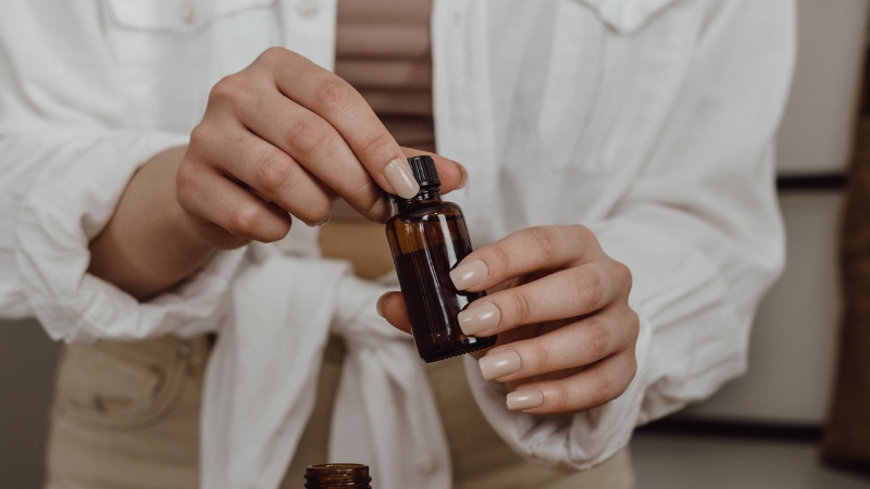 Close-up of a woman opening a small amber bottle of essential oil during an aromatherapy routine