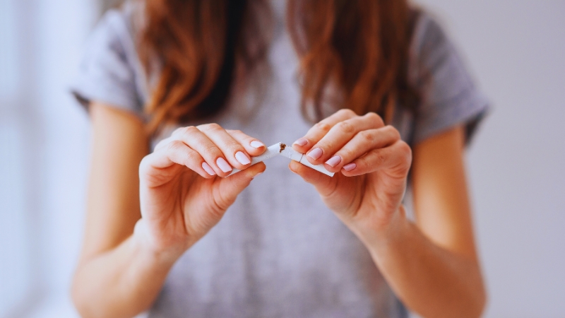 A woman breaks a cigarette in half with both hands, symbolizing quitting smoking