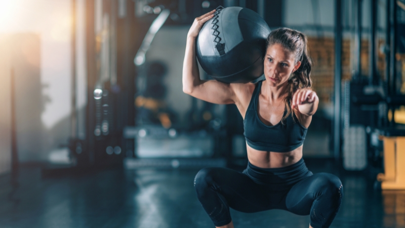 Woman performing a squat with a weighted ball during a gym workout, showing how strength training can impact blood sugar levels