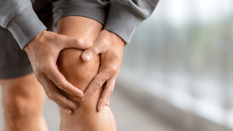 Close-up of a person holding their knee in discomfort, suggesting joint pain or strain.